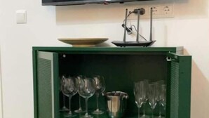 Une pièce dotée d’un téléviseur à écran plat fixé au mur, au-dessus d’un meuble vert muni d’étagères où sont rangés des verres à vin et des carafes.