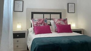 Une chambre à coucher comprenant un lit, deux tables de chevet, une tête de lit et deux appliques murales.