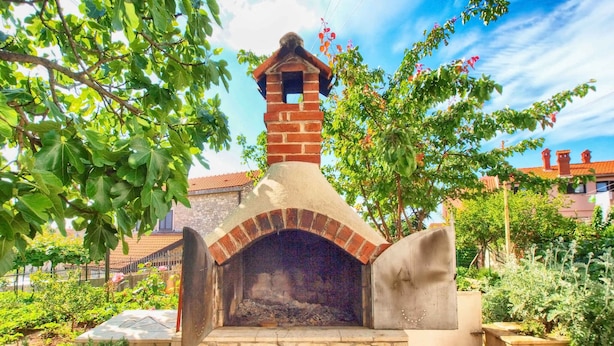 A brick-built outdoor oven with a chimney, surrounded by greenery and a stone wall. - Holiday apartment with air conditioning (Pula)