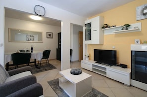 A living room with a TV, sofa, dining table, chairs, and a small coffee table.