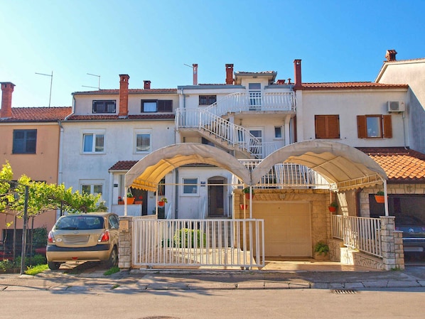 A residential building with a gated entrance, a covered porch with a metal railing, and a car parked in front.
