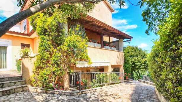 A two-story house with a stone-paved courtyard, a balcony with potted plants, and a clear blue sky. - Holiday apartment with air conditioning (Pula)