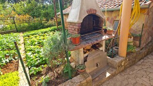 An outdoor brick oven with a chimney, surrounded by a garden with various plants and a stone pathway. - Holiday apartment with air conditioning (Pula)