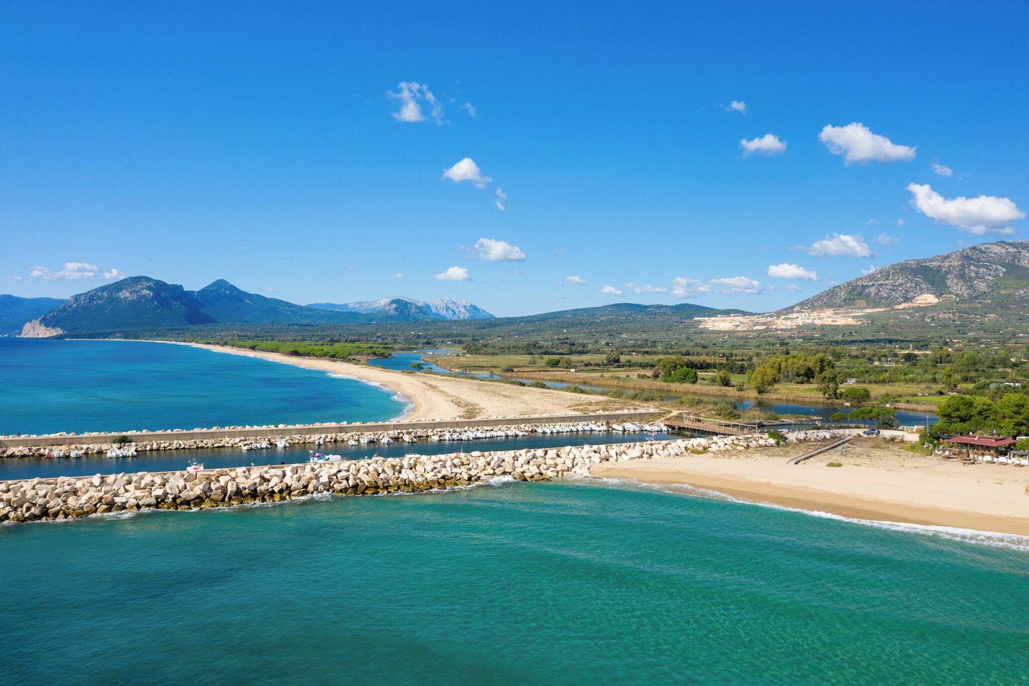 Un paisaje costero con playa, aguas azul turquesa y montañas al fondo.