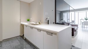 Une cuisine moderne dotée d’un grand îlot central, d’un coin repas avec un canapé et des fauteuils, et offrant une vue à travers un mur de verre.