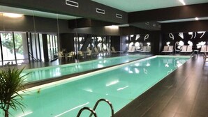 Une piscine à l’eau claire, entourée d’un revêtement de sol foncé, et un espace détente avec des chaises et des tables.