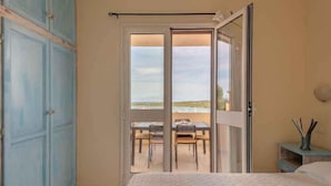 A bedroom with a large bed, a sliding glass door leading to a balcony with a table and chairs, and a wardrobe. - Holiday apartment With a view of the sea (Golfo Aranci)