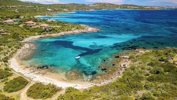 An aerial view of a coastal area with clear turquoise waters, a sandy beach, and scattered buildings. - Holiday apartment With a view of the sea (Golfo Aranci)
