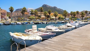 A marina with boats docked, a wooden dock, and buildings with palm trees in the background. - Holiday apartment With a view of the sea (Golfo Aranci)