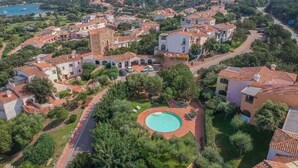 Vista aérea de uma área residencial costeira com casas em terraços, uma piscina central e vista clara do mar.