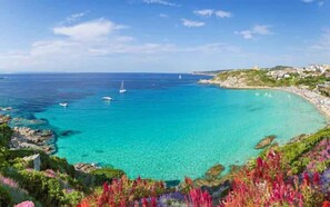 Vista costeira com águas turquesa cristalinas, barcos e um litoral rochoso com vegetação.