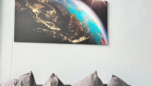 A modern living room with a grey sofa, a glass coffee table, and a large wall-mounted picture of Earth at night.