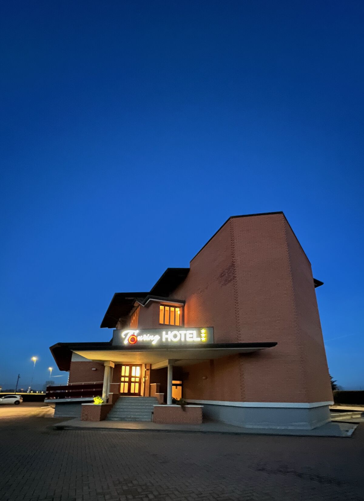 Un hôtel dont l’enseigne, bien visible, porte l’inscription « Hôtel avec service de dépannage » et qui est illuminée au crépuscule.