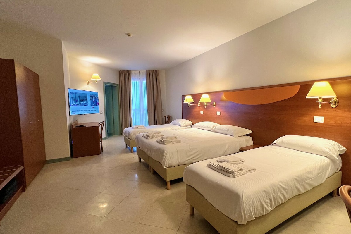 A hotel room with two beds, a desk, a TV, and a bathroom.