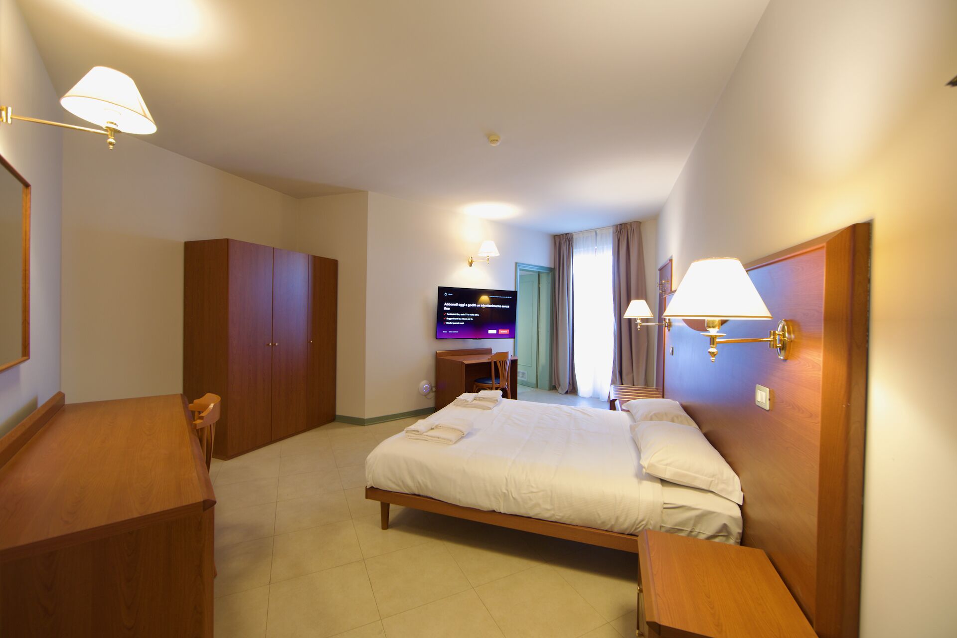 Una habitación de hotel con cama, escritorio, silla, armario y televisor.