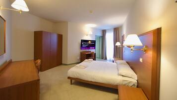 Una habitación de hotel con cama, escritorio, silla, armario y televisor.