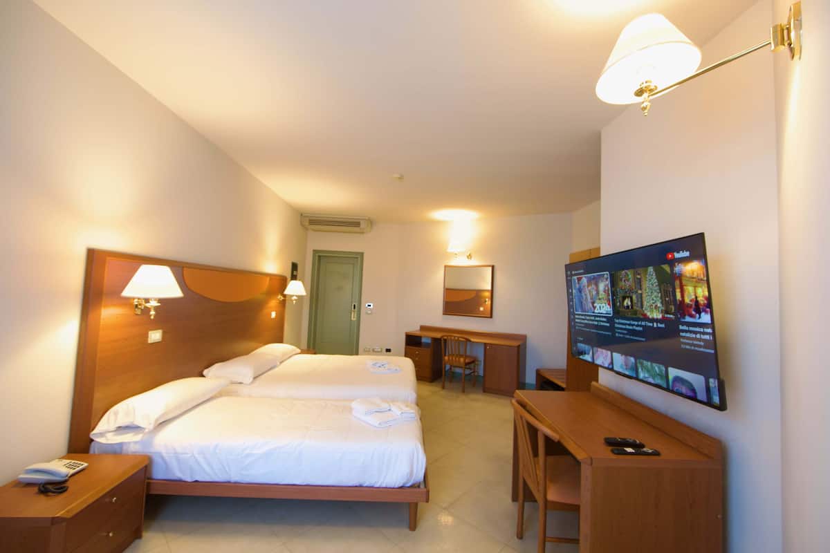 A hotel room with two beds, a desk, a chair, a TV, and a lamp.