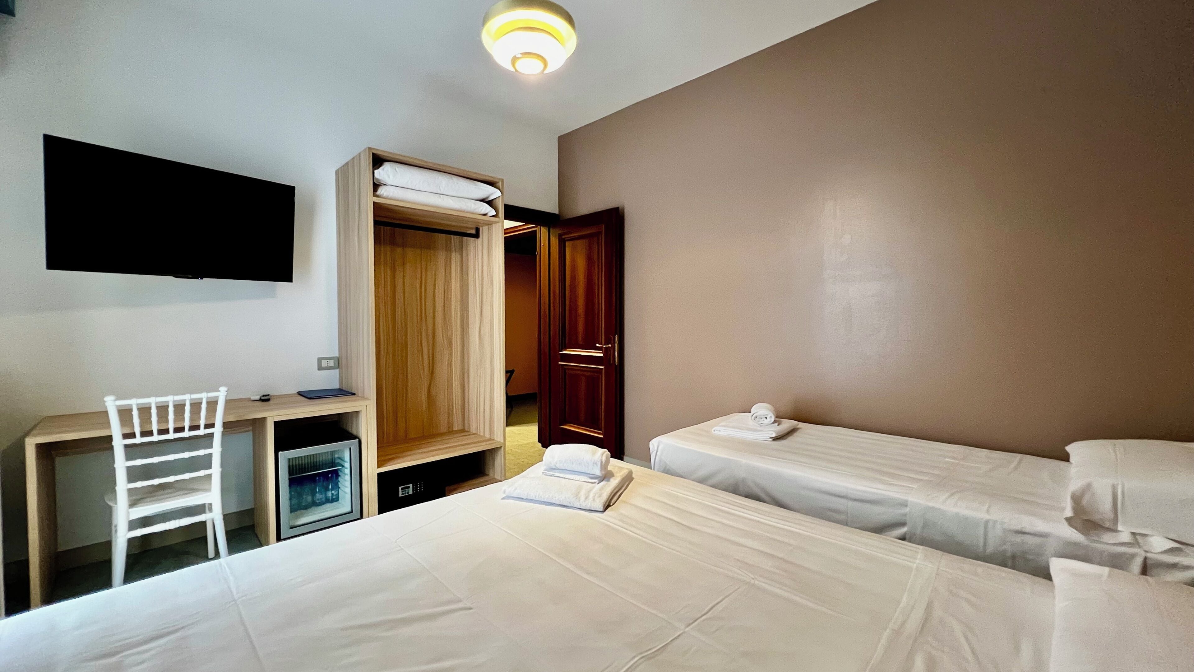 Une chambre d’hôtel comprenant un lit, un bureau avec une chaise, une télévision et une armoire.