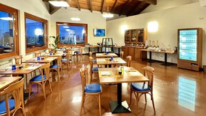 A spacious dining area with wooden tables and chairs, large windows, and a high ceiling with exposed beams. - HC Hotel Touring Seniga (Seniga)