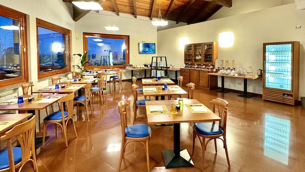 Un comedor amplio con mesas y sillas de madera, ventanas grandes y un techo alto con vigas a la vista.