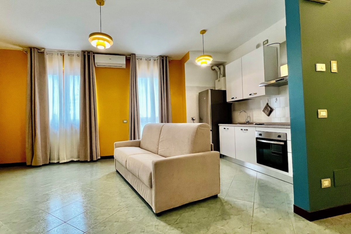 A living room with a sofa, a kitchen with cabinets and appliances, and a dining area with a table and chairs.