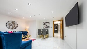 Un salon moderne avec un canapé bleu, un téléviseur à écran plat et un coin repas comprenant une table et des chaises.