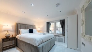 Une chambre à coucher avec un grand lit, des lampes de chevet, une fenêtre avec des rideaux et un radiateur.