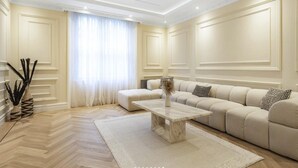 A modern living room with a beige sofa, a marble coffee table, and a large window with sheer curtains. - Luxury One-bedroom in Central London (London)