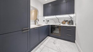 A modern kitchen with dark cabinets, a marble countertop, and built-in appliances. - Luxury One-bedroom in Central London (London)