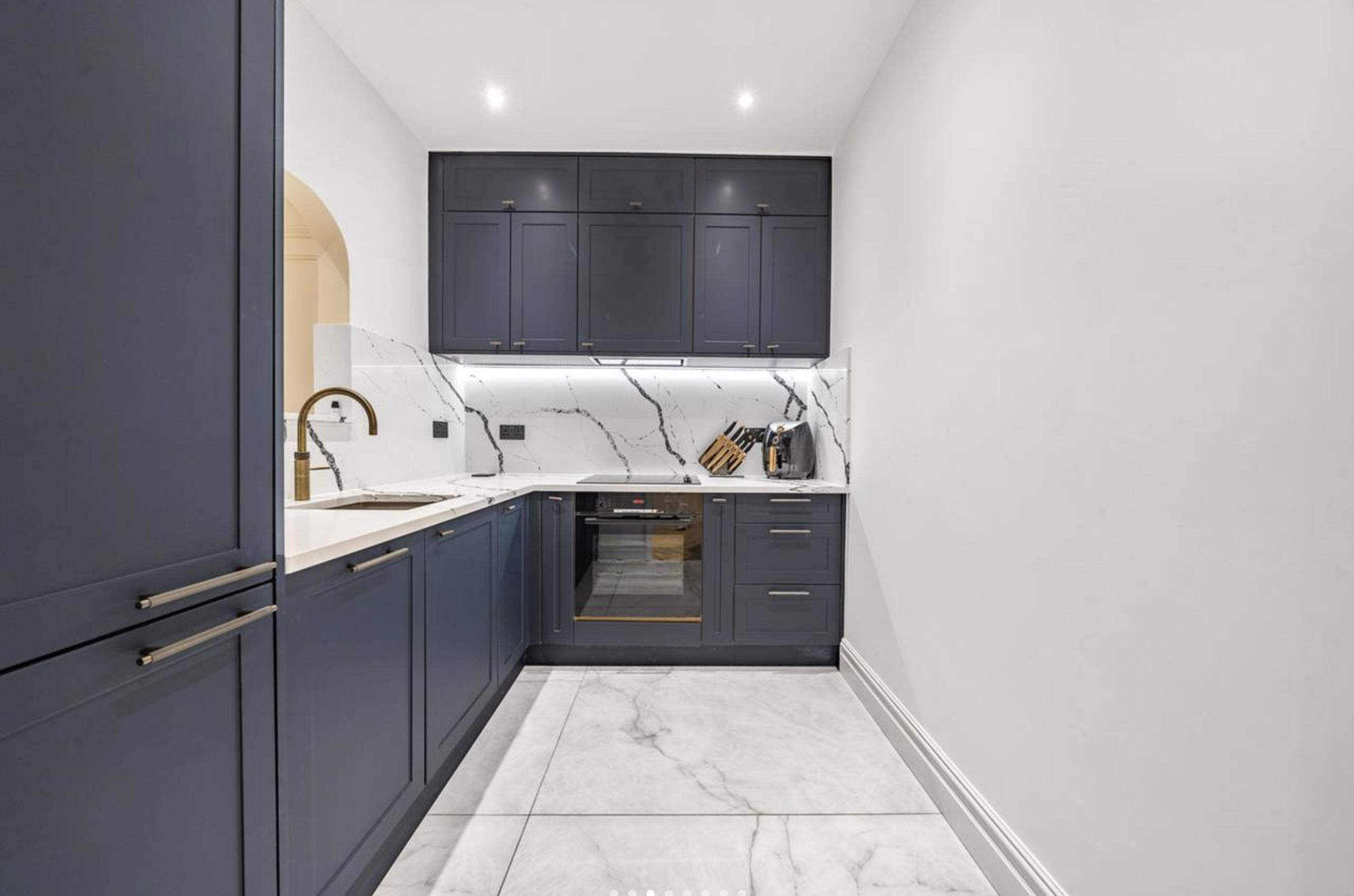 Une cuisine moderne avec des meubles de couleur sombre, un plan de travail en marbre et un four.