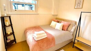 Ein Schlafzimmer mit Bett, Fenster, Nachttisch, Lampe und einem Bild an der Wand.