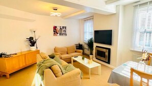 Ein Wohnzimmer mit einer Couch, Couchtisch, Fernseher, Kamin und einem Essbereich mit Tisch und Stühlen.