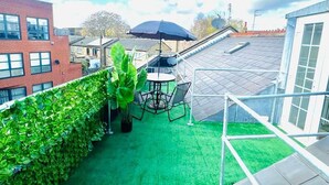 Eine Dachterrasse mit künstlichem Rasen, einem Tisch mit Stühlen und einem schwarzen Sonnenschirm.