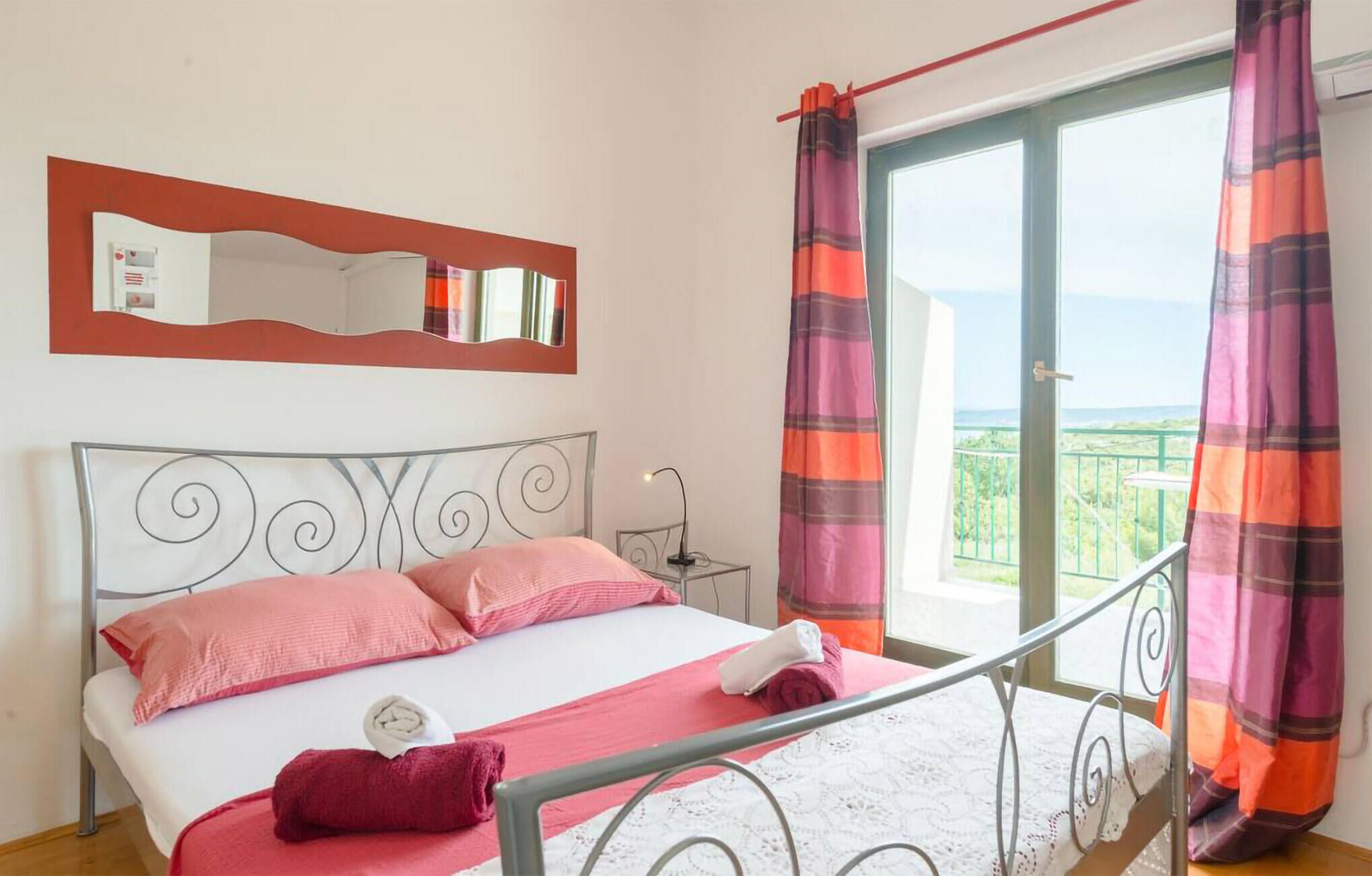 Une chambre à coucher avec un lit, une table de chevet, un miroir et une vue sur l’extérieur.