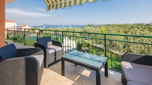 Un balcon agrémenté de meubles en osier, d’une table en verre et offrant une vue sur un vignoble et un paysage lointain.