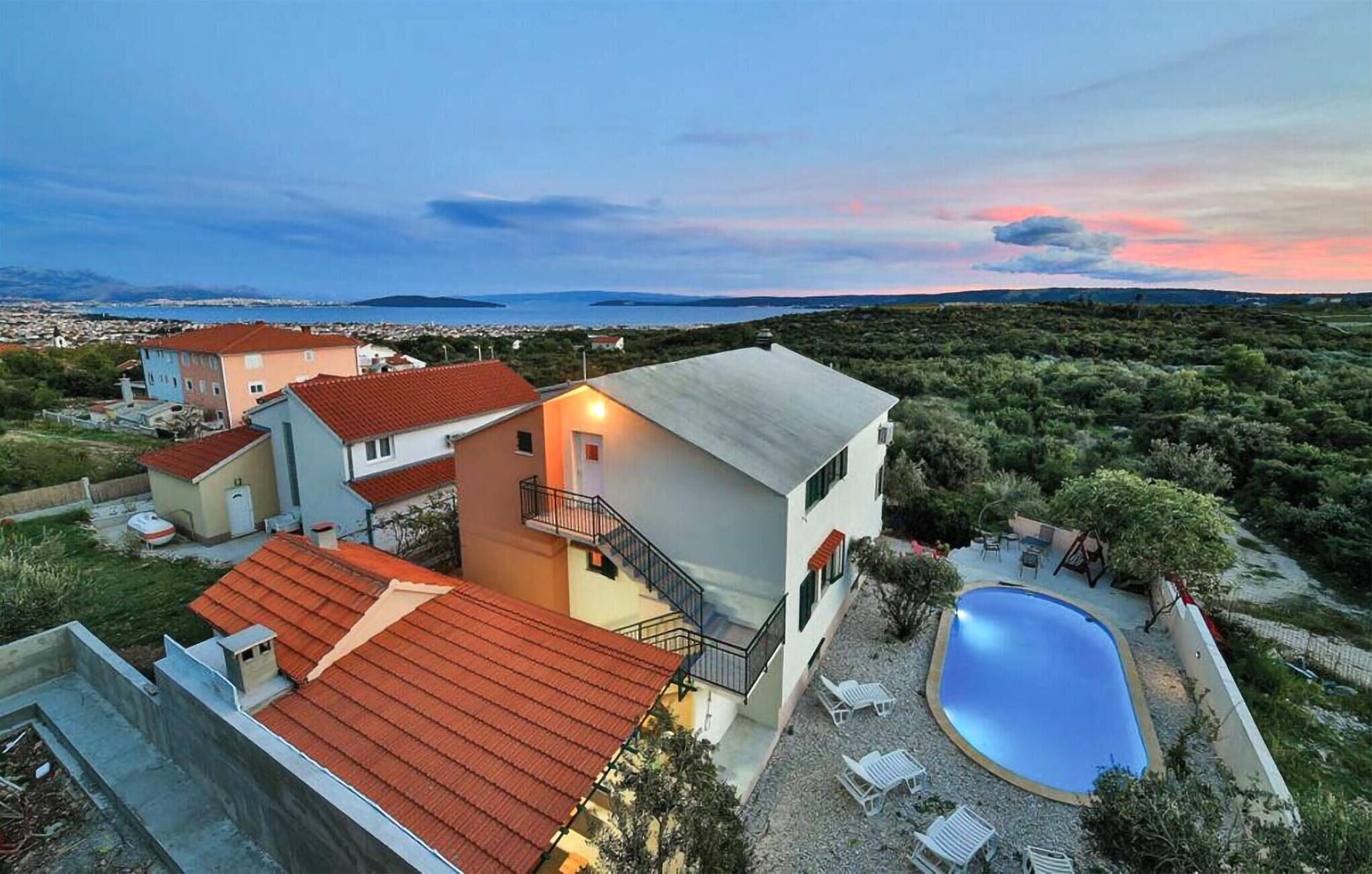 A modern villa with a swimming pool, surrounded by lush greenery and a scenic view of the sea.