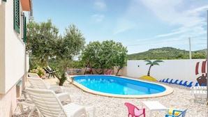 Une piscine bordée de chaises longues blanches, d’une petite table et de chaises colorées.