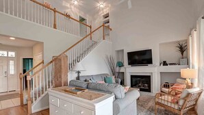 A spacious living room with a staircase, a fireplace, and a television.