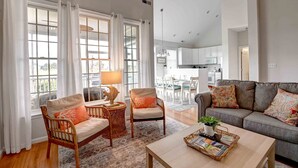 A spacious living room with a grey sofa, wicker chairs, a coffee table, and a dining area in the background.