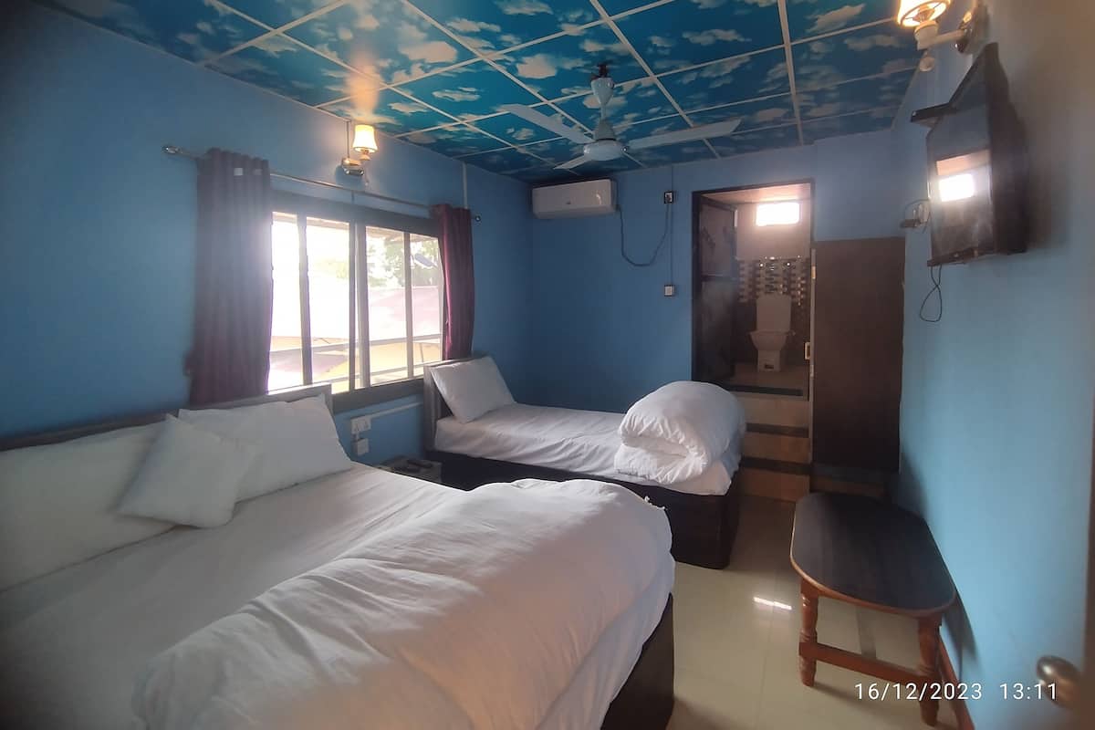A room with two beds, a ceiling fan, a window with curtains, a door leading to a bathroom, and a small wooden chair.