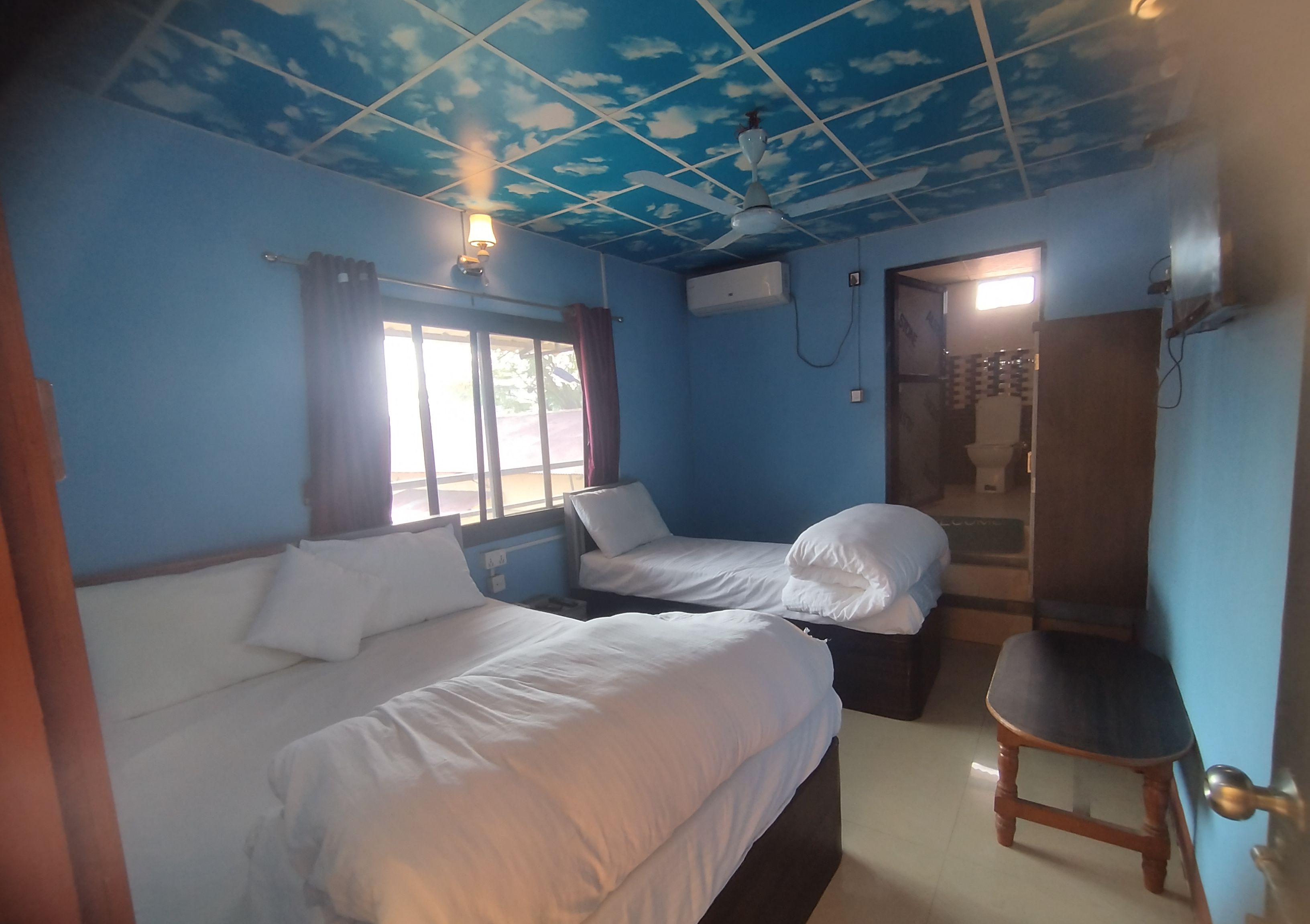 A room with two beds, a ceiling fan, and a window with curtains.