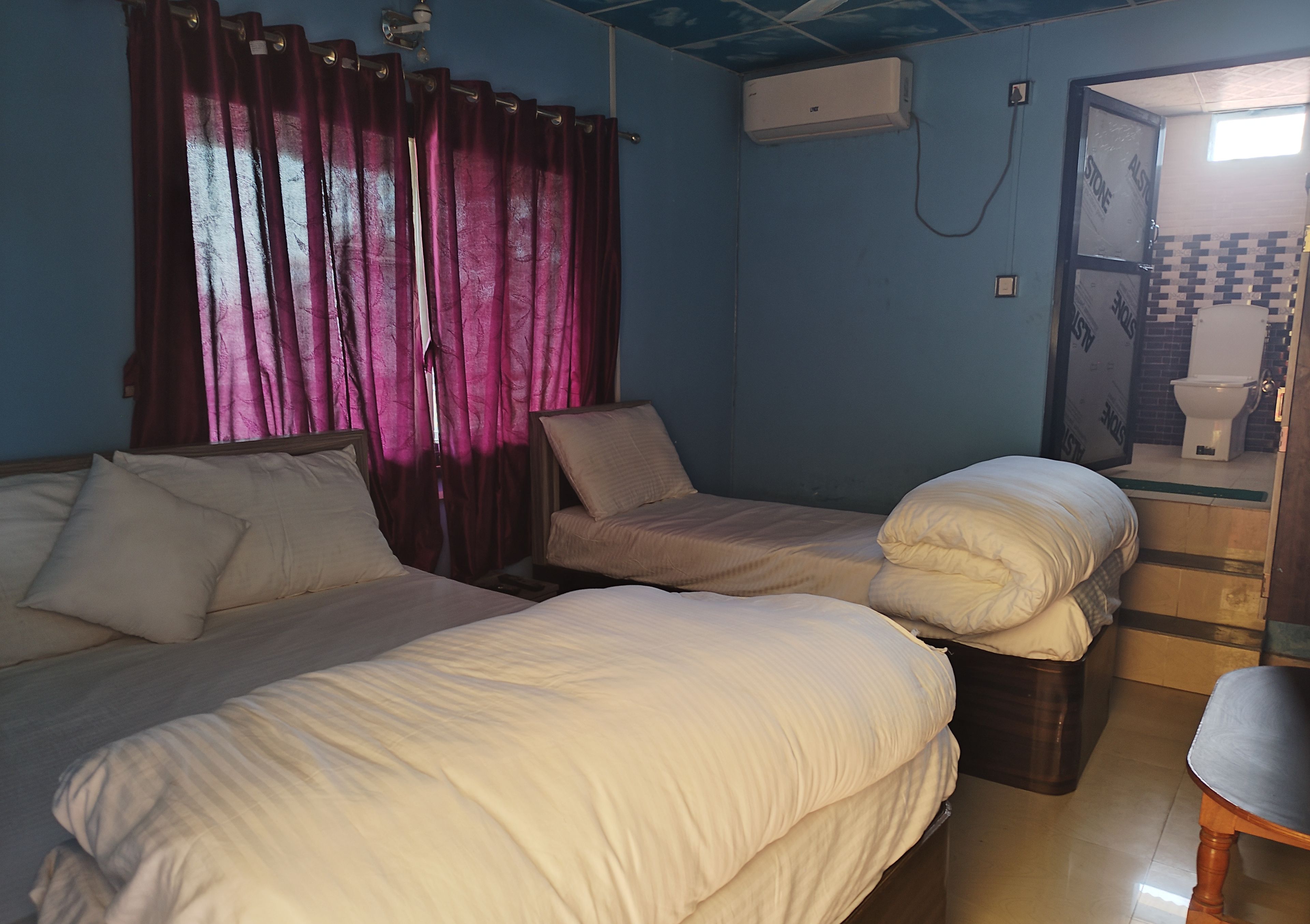 A room with two beds, a wooden chair, a small table, and a bathroom visible through an open door.