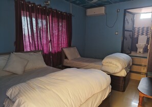 A room with two beds, a wooden chair, a small table, and a bathroom visible through an open door.