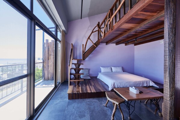 A room with a bed, a wooden table, and a staircase leading to an outdoor balcony. - Kenting Singhaiwan (Hengchun)