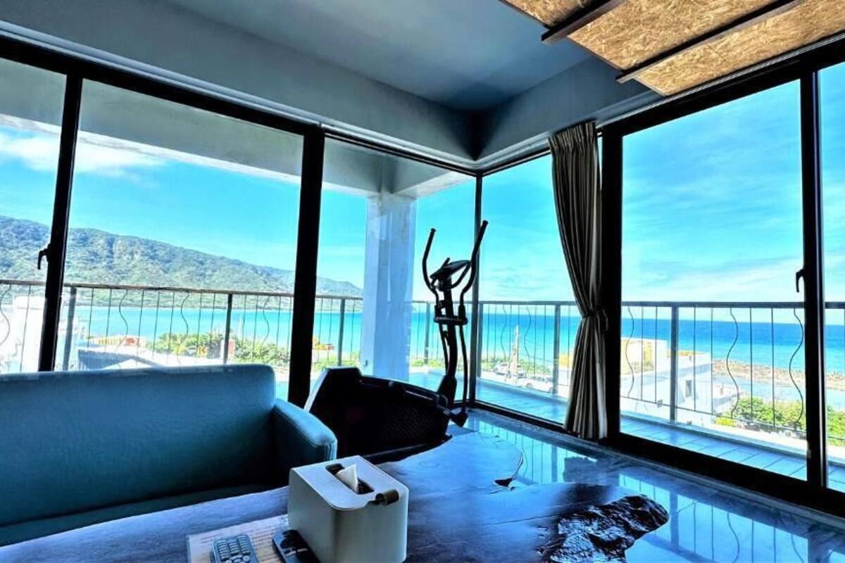 A room with a large window offering a view of the sea and mountains.