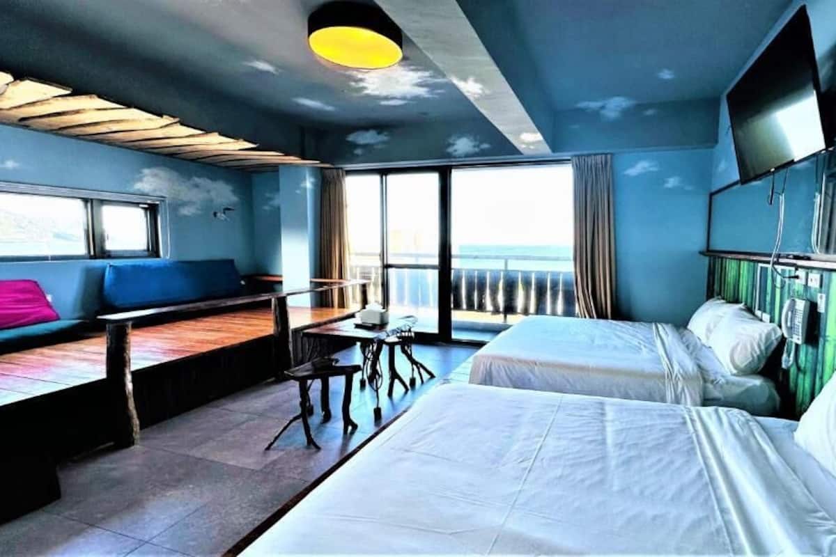A hotel room with two beds, a desk, a chair, and a large window with a view.