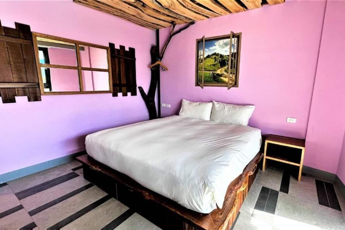 A bedroom with a wooden bed frame, a large mirror, and a painting on the wall.