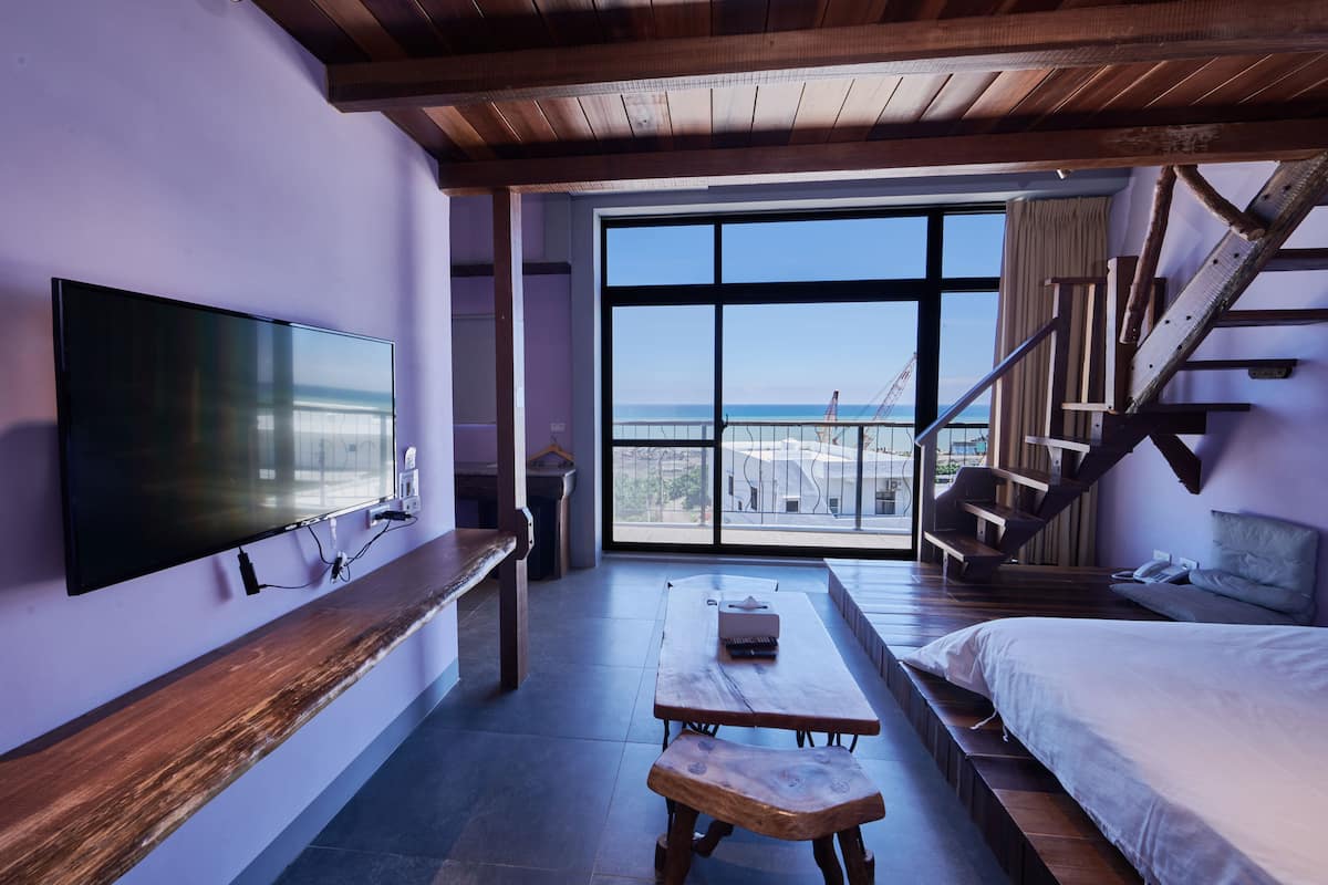 A room with a large TV, wooden bench, and a bed.