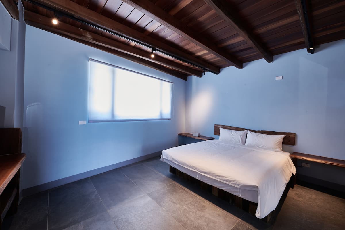 A bedroom with a wooden bed, a nightstand, a window, and a ceiling with exposed beams.