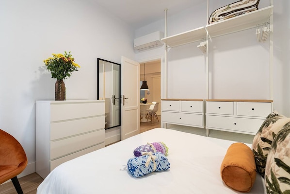 A bedroom with a bed, a dresser, a chair, a bedside table, and a door leading to another room.